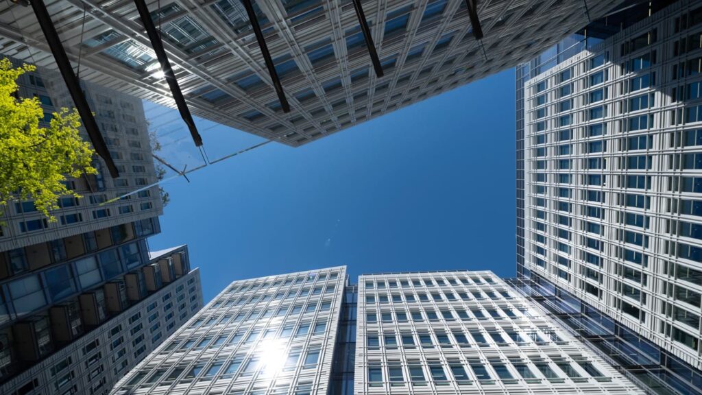 looking up at silver tall buildings from ground level with a blue sky