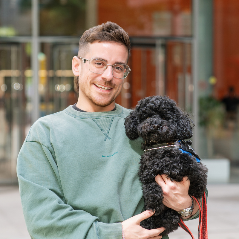 man in a grey sweatshirt and glasses holding a black poodle dog