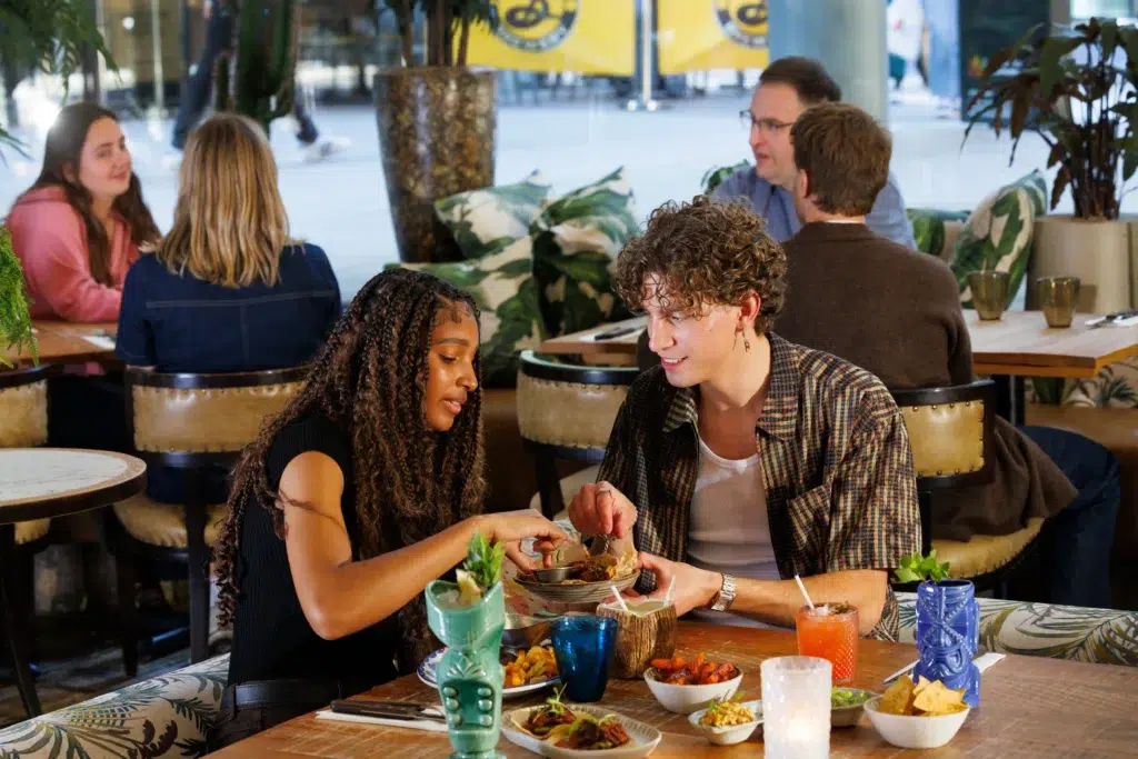a man and woman enjoying a meal together with cocktails and food laid out before them