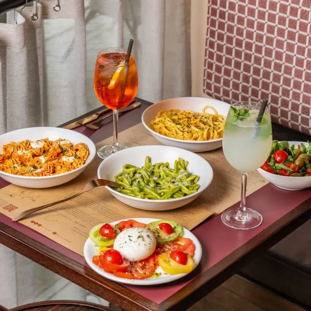 handmade pasta dishes and spritz drinks laid out on a dark woof table with